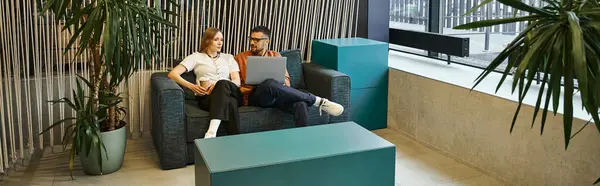 Два сотрудника расслабляются и болтают на диване в современном рабочем пространстве, отражая динамичный образ жизни стартапов. — стоковое фото