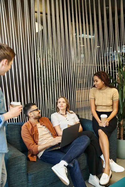 A creative startup team of colleagues shares innovative ideas while perched atop a couch in a modern coworking space. — Stock Photo