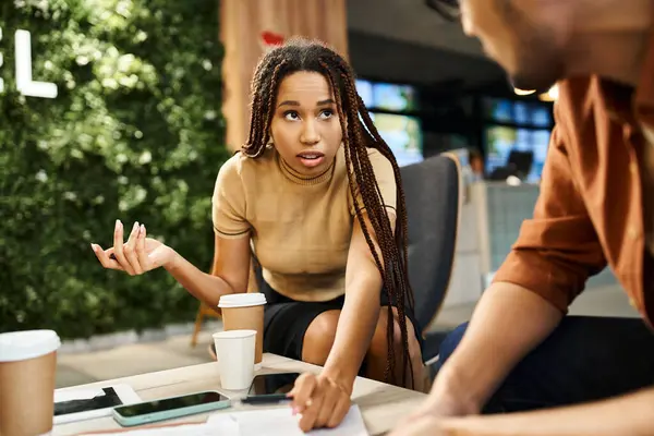 Una mujer y un hombre participan en una conversación en una mesa, discutiendo estrategias de inicio en un entorno empresarial moderno. - foto de stock