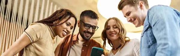 A group of colleagues in a coworking space huddle together, captivated by the content on a smartphone screen. — Stock Photo