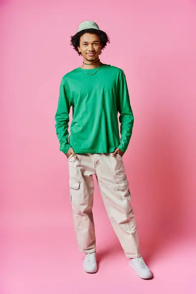 Ein fröhlicher junger afroamerikanischer Mann mit lockigem Haar trägt lässig grünes Hemd und khakifarbene Hose vor rosa Hintergrund. — Stockfoto