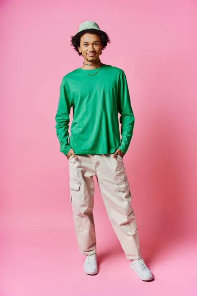 A cheerful young African American man with curly hair wearing casual green shirt and khaki pants against a pink background. — Stock Photo