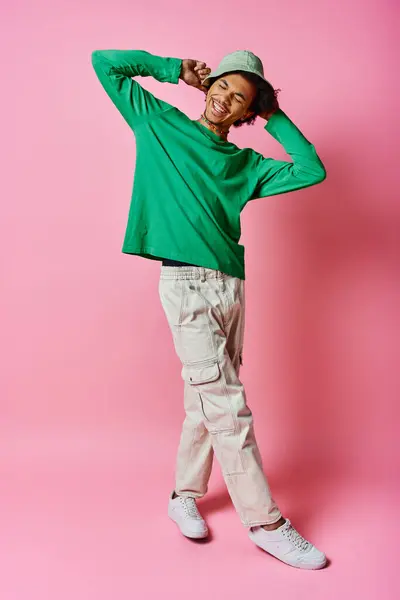 Cheerful African American man with curly hair, wearing a green shirt and white pants, exuding emotion on a pink background. — Stock Photo