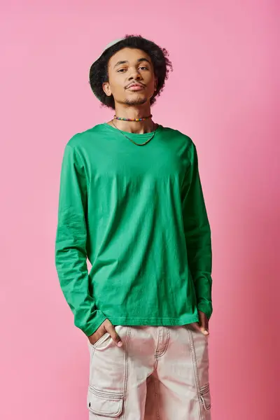 A cheerful young African American man, with curly hair, stands confidently in front of a pink wall. — Stock Photo