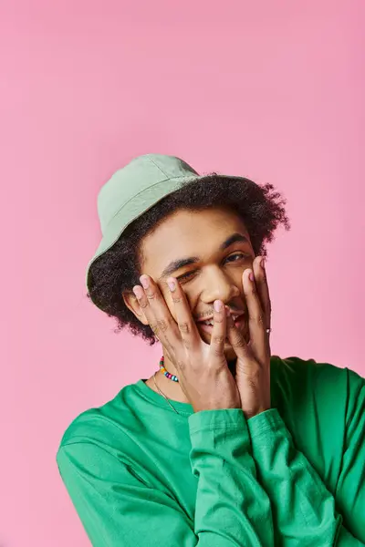 Ein fröhlicher, junger, lockiger Afroamerikaner trägt ein grünes Hemd und einen Hut vor rosa Hintergrund. — Stockfoto