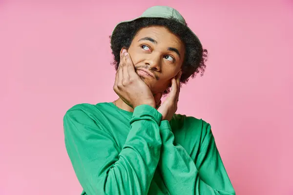 A pensive young African American man in a green shirt strikes a pose against a pink background. — Stock Photo