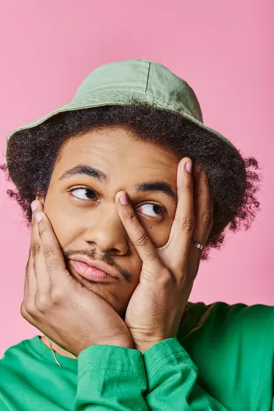 Ein nachdenklicher afroamerikanischer Mann in Freizeitkleidung, mit lockigem Haar, mit grünem Hemd und Hut auf rosa Hintergrund. — Stockfoto
