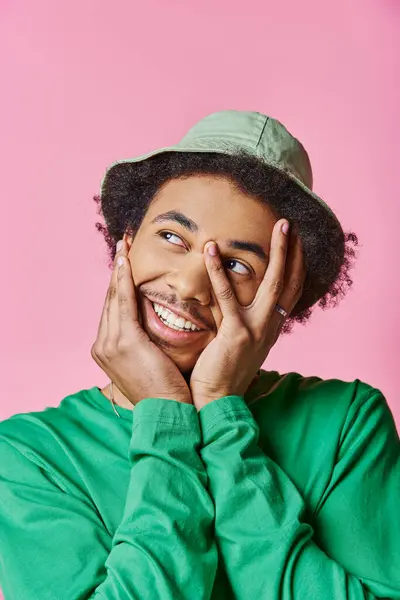 A cheerful young African American man with curly hair, and green shirt on a pink background. — Stock Photo