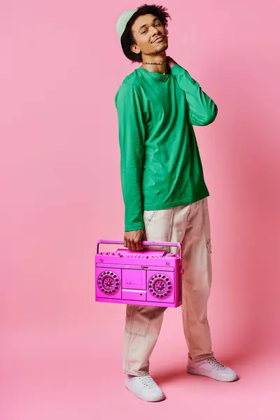 Cheerful African American man in green shirt holding pink radio on pink background, displaying emotions. — Stock Photo