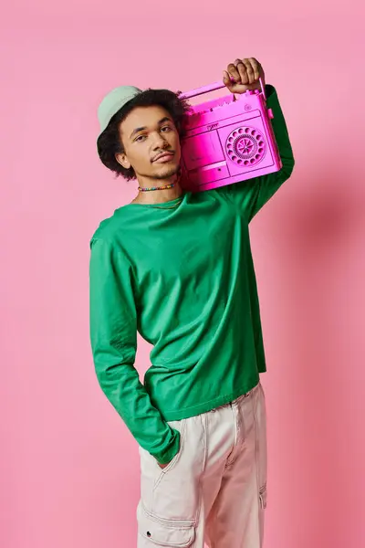 Um jovem afro-americano alegre com uma camisa verde segurando uma boombox rosa em um fundo rosa. — Fotografia de Stock