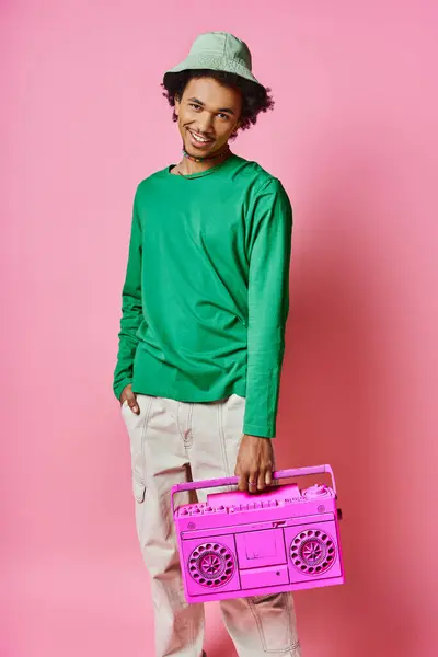 Curly African American man in a green shirt joyfully holding a pink radio on a pink background. — Stock Photo