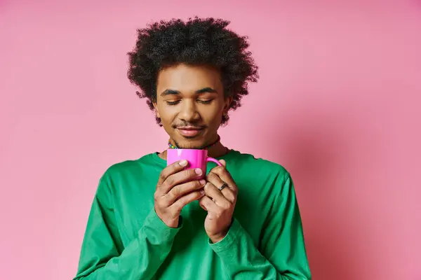 Fröhlicher afroamerikanischer Mann mit lockigem Haar im grünen Hemd, der eine rosa Tasse in der Hand hält und Emotionen ausdrückt. — Stockfoto