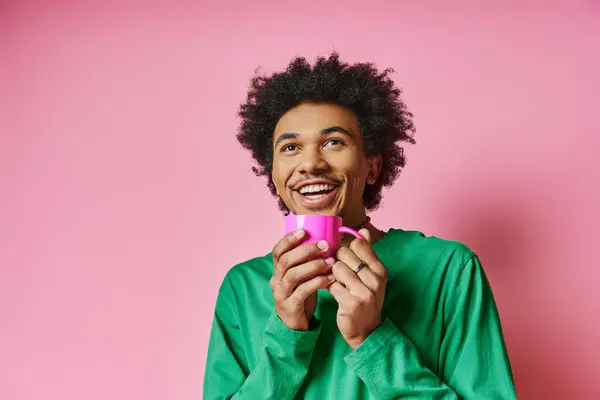 Un jeune homme afro-américain joyeux en tenue décontractée tenant une tasse rose sur un fond rose vibrant. — Photo de stock