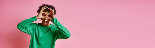 Fröhlicher junger afroamerikanischer Mann in grünem Hemd, der seine Augen verhüllt und seinen Emotionen Ausdruck verleiht, auf rosa Hintergrund. — Stockfoto