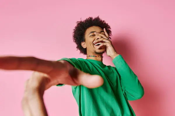 A cheerful young African American man in a green shirt smiling on a pink background. — Stock Photo