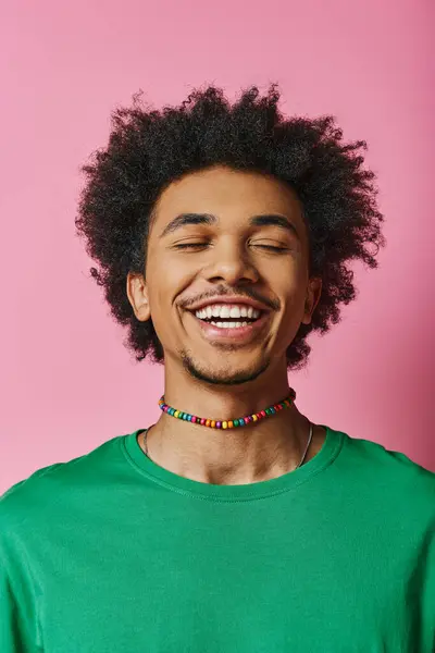 A cheerful young African American man with curly hair and casual attire smiles brightly against a pink background. — Stock Photo