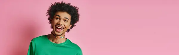Ein fröhlicher junger afroamerikanischer Mann mit lockigem Haar, lässig in grünem Hemd, lächelnd auf rosa Hintergrund. — Stockfoto