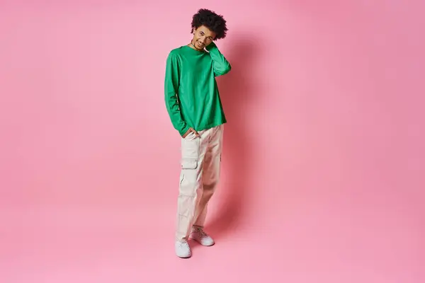 A cheerful young African American man in a green sweater stands against a pink background, exuding emotion. — Stock Photo
