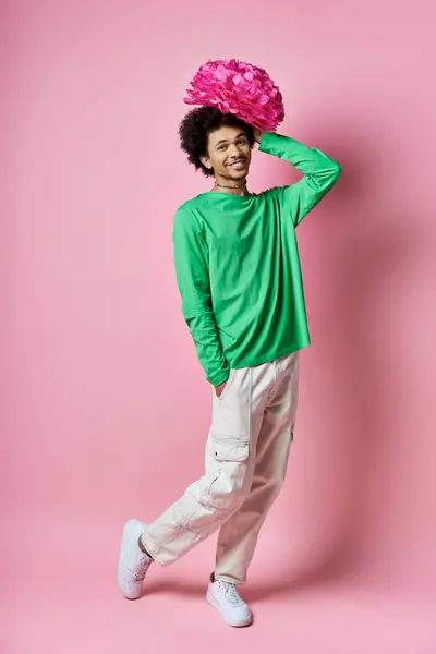 Um jovem afro-americano alegre com uma camisa verde e calças brancas, com uma flor rosa na cabeça, contra um fundo rosa. — Fotografia de Stock