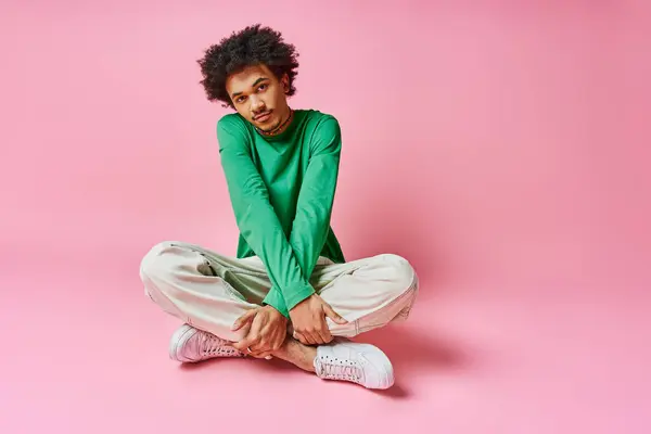 A cheerful young African American man with curly hair sits cross-legged on the ground, deep in thought. — Stock Photo