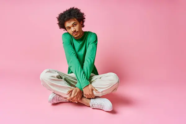 Un allegro giovane afroamericano dai capelli ricci siede a gambe incrociate a terra, profondamente pensieroso. — Foto stock