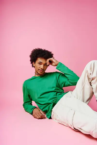 Homme afro-américain joyeux aux cheveux bouclés en chemise verte décontractée et pantalon blanc, exprimant des émotions sur fond rose. — Photo de stock