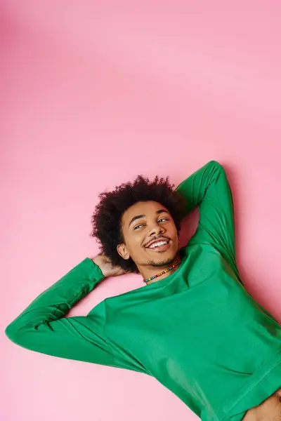 A cheerful curly African American man in a green shirt laying peacefully on a vivid pink background. — Stock Photo