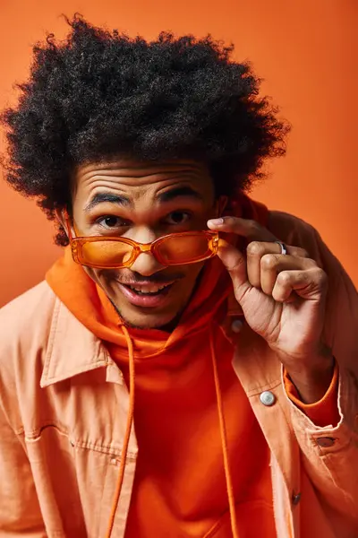 Trendy African American man with curly afro hair and sunglasses posing expressively in an orange shirt. — Stock Photo
