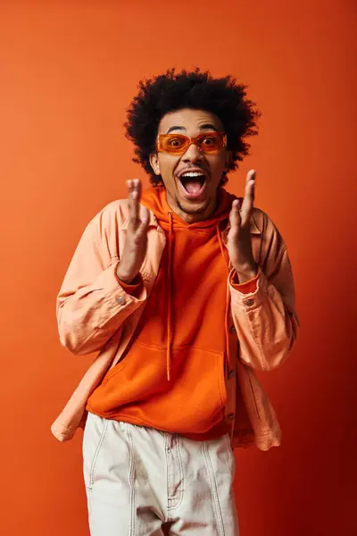 Um jovem afro-americano elegante em uma camisa laranja e shorts brancos exala emoções contra um fundo laranja. — Fotografia de Stock