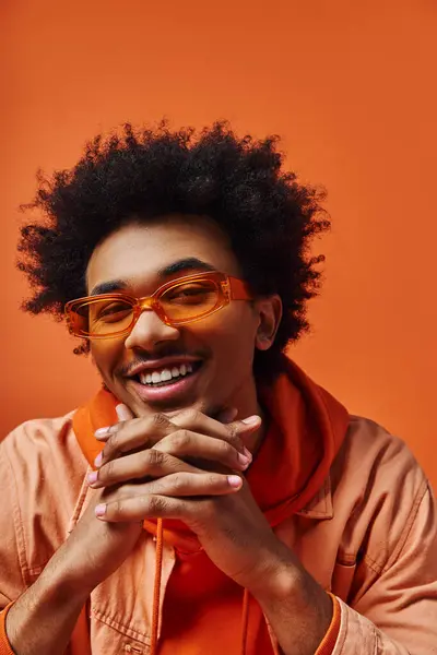 Jovem afro-americano com cabelo encaracolado vestindo óculos e uma camisa laranja contra um fundo vibrante. — Fotografia de Stock