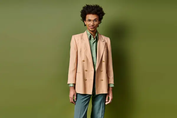 Stylish young curly African American man in a suit standing confidently in front of a vivid green wall. — Stock Photo