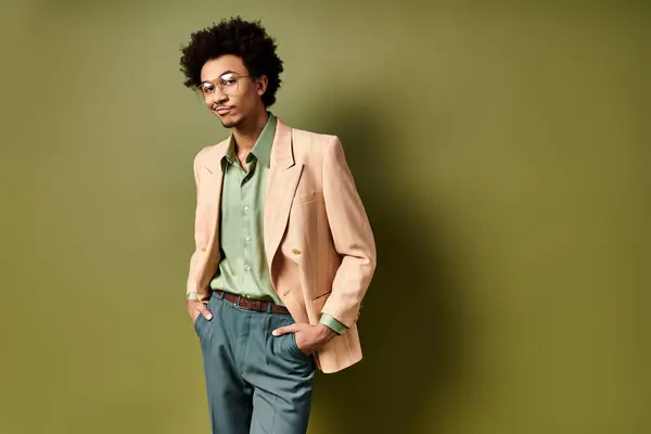 A young African American man, stylishly dressed, stands confidently in front of a vibrant green wall, wearing trendy sunglasses. — Stock Photo