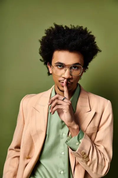 Un giovane afroamericano alla moda in tuta e occhiali colpisce una posa sicura su uno sfondo verde vibrante. — Foto stock