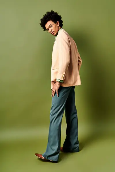 Um homem afro-americano da moda com cabelos encaracolados e óculos de sol em pé com confiança na frente de uma parede verde vibrante. — Fotografia de Stock