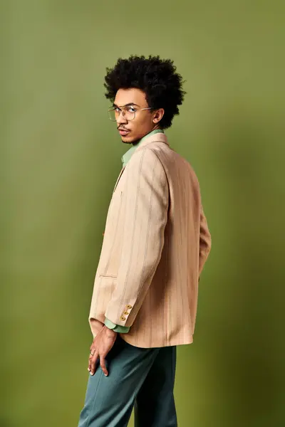 Stylish African American man with curly hair and glasses, exudes confidence in trendy suit against green background. — Stock Photo