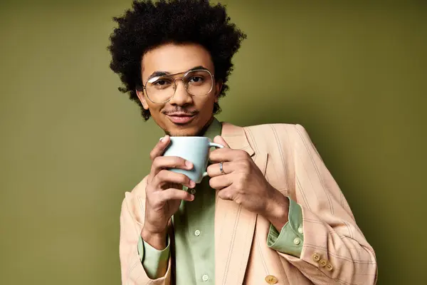 Un giovane afroamericano alla moda con capelli ricci e occhiali da sole tiene una tazza fumante di caffè su uno sfondo verde. — Foto stock