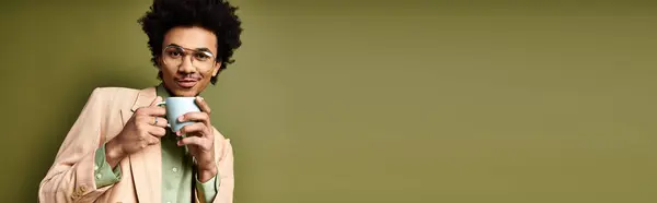 Young African American man with curly hair and trendy attire holding a cup in his right hand, wearing sunglasses on a green background. — Stock Photo