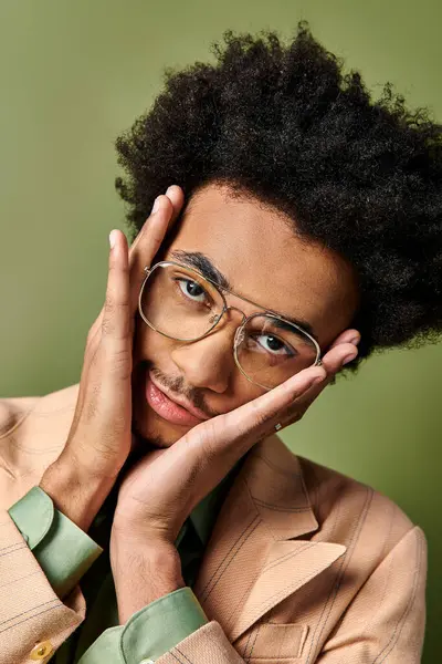 A stylish, young, African American man with curly hair and trendy attire striking a pose for a photo on a green background. — Stock Photo