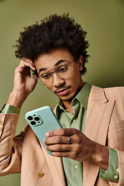 Stylish young African American man in a suit and sunglasses confidently holding a cell phone against a green background. — Stock Photo