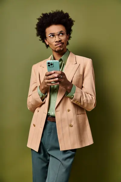 Elegante giovane uomo afroamericano in abiti alla moda e occhiali da sole prendere un selfie con il suo telefono cellulare su sfondo verde. — Foto stock