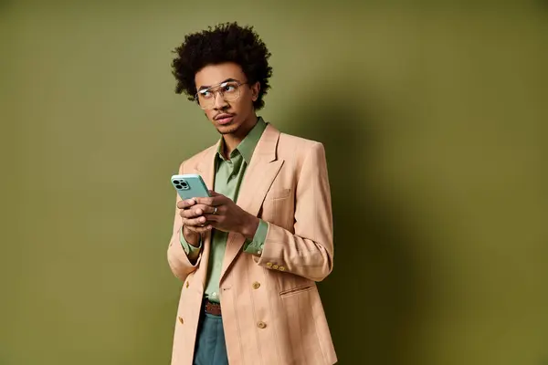 A stylish young African American man in a suit and sunglasses, confidently holding a cell phone against a green background. — Stock Photo