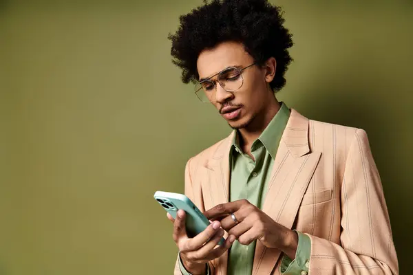 A stylish young African American man in a suit and sunglasses, using a cell phone on a green background. — Stock Photo