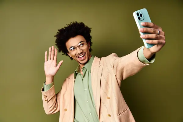 Junger Afroamerikaner in schickem Anzug und Sonnenbrille macht ein Selfie mit einem Handy auf grünem Hintergrund. — Stockfoto