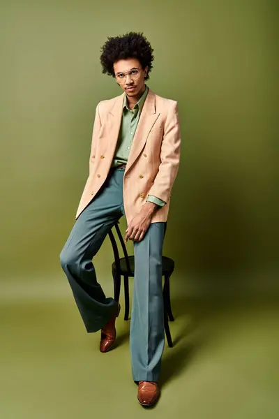 A stylish young African American man in a suit and sunglasses confidently sits atop a chair against a vibrant green background. — Stock Photo