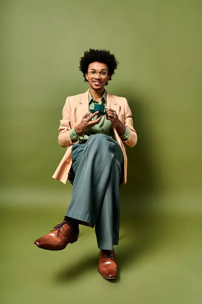 Stylish African American man in suit and sunglasses holding a cup of coffee against a green background. — Stock Photo