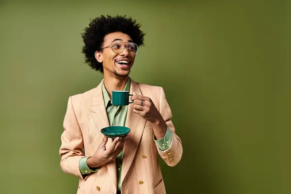 Стильний молодий афроамериканський чоловік у костюмі та сонцезахисних окулярах, тримає чашку кави на зеленому фоні. — стокове фото
