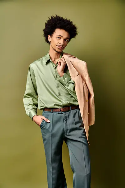 Um jovem afro-americano elegante com cabelo encaracolado, vestindo uma camisa verde e calças azuis, posa com confiança contra um fundo verde. — Fotografia de Stock
