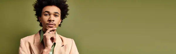 A stylish young African American man with curly hair wearing a suit, exuding confidence and sophistication on a green background. — Stock Photo