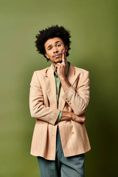 Young African American man in trendy attire standing with hands on chin in thoughtful pose on green background. — Stock Photo