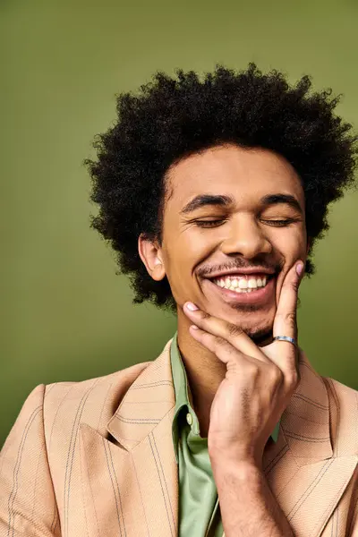Стильний молодий афроамериканський чоловік з кучерявим волоссям і модним вбранням, посміхаючись для камери на яскравому зеленому фоні. — стокове фото